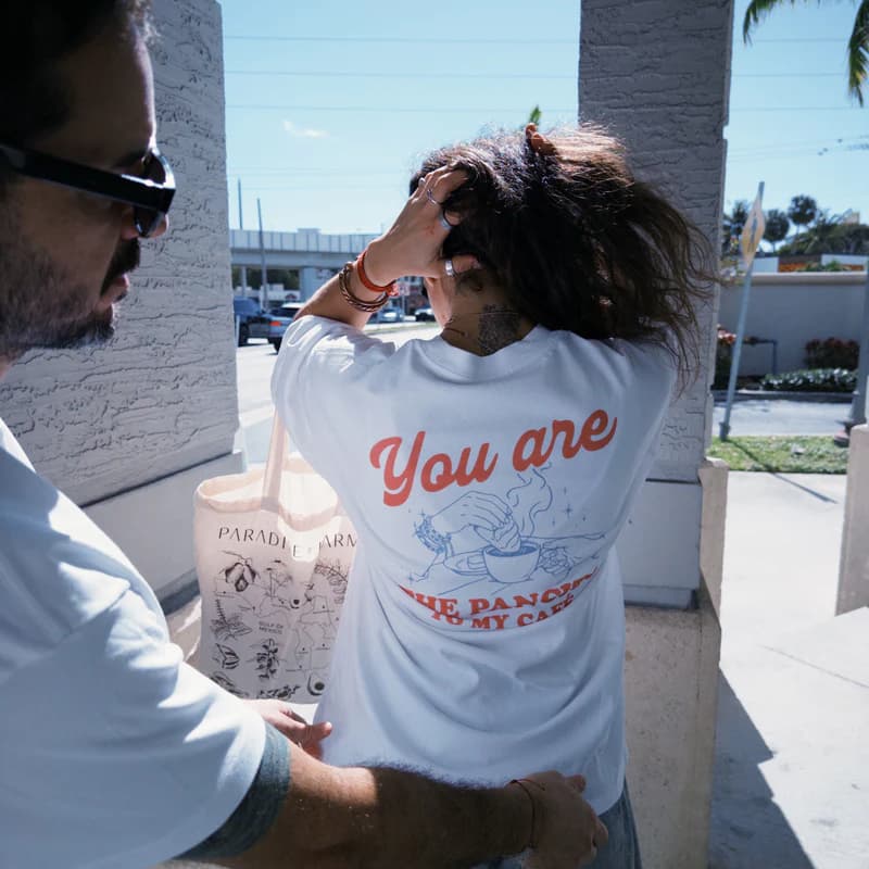 Un homme montrant l'arrière d'un T-Shirt imprimé sur une jeune femme tatouée